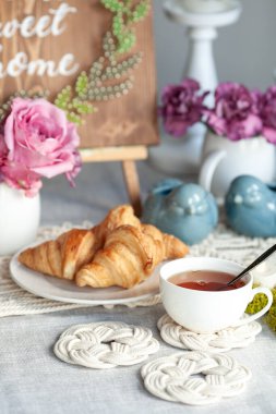 Güzel sıcak kahvaltı, kruvasan ve çay, masa makrome peçetelerle süslenmiş.