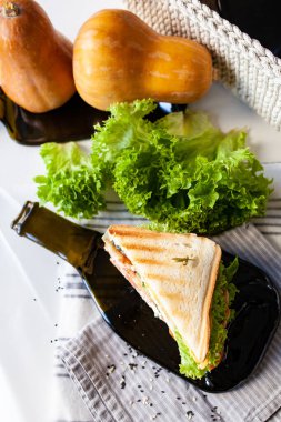 Peynirli sandviç, domates, salatalık ve jambonlu. Koyu bir şişeden alınmış cam bir tabakla. Hafif arkaplan