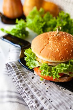 Peynirli Caprese burger, domates, salatalık ve jambon. Koyu bir şişeden alınmış cam bir tabakla. Hafif arkaplan