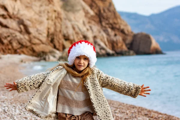 Deniz Kıyısında Noel Baba Şapkalı Küçük Güzel Kız Ceketli Bir — Stok fotoğraf