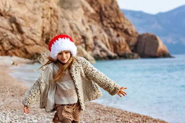 Deniz Kıyısında Noel Baba Şapkalı Küçük Güzel Kız Ceketli Bir — Stok fotoğraf