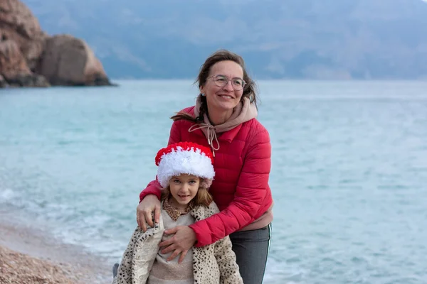 Anne Kız Noel Baba Nın Şapkasıyla Sahil Boyunca Yürüyorlar Gülüyorlar — Stok fotoğraf