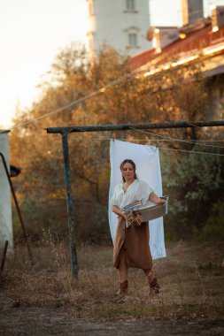 Uzun saçlı güzel bir kadın deniz fenerinin yanındaki havaya beyaz çarşaflar asıyor. Sıcak bir sonbahar günü, günbatımı, akşam, açık hava.