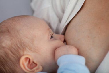 Güzel bir kadın bir bebeği arka planda beyaz çarşaflarla emziriyor.