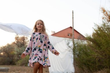 Beyaz çarşafların arkasında hoş bir kız. Sonbaharda gün batımında, kırsal kesimde bir çocuk elbiseyle yürüyor.