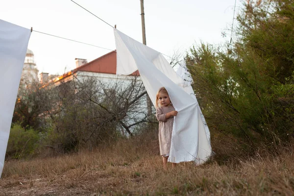 秋天的日落时分 一个小女孩穿着一件衣服 站在乡村 背对着白色的被单 — 图库照片