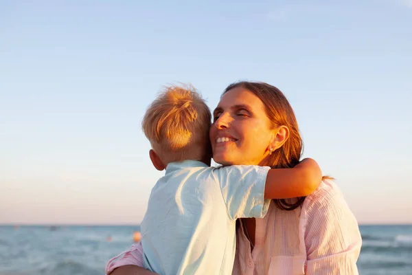 妈妈和她的儿子拥抱在一起 微笑着看着蓝色的海景 — 图库照片