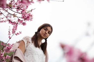 Bahar şeftali bahçesinde güzel bir kız. Yağmurluk ve kot giyen bir genç.