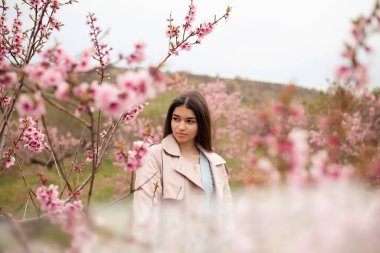 Bahar şeftali bahçesinde güzel bir kız. Yağmurluk ve kot giyen bir genç.