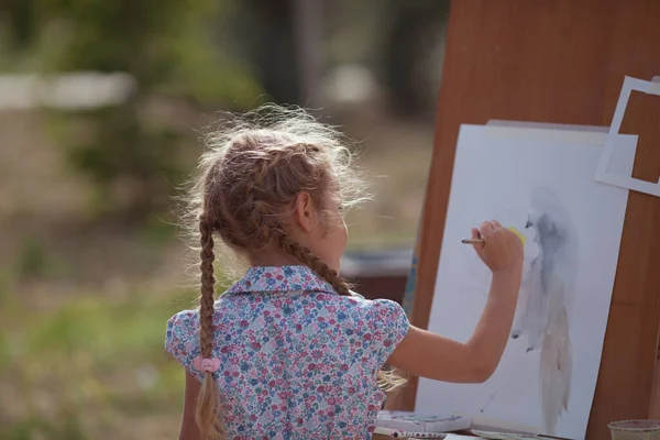 The girl draws in the park on an easel, plein air. Child learns to draw in nature