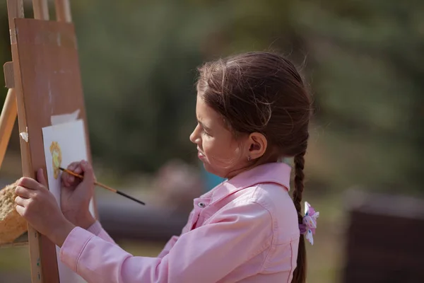 少女はイーゼルの上の公園で空中で絵を描く 子供は自然に描くことを学ぶ — ストック写真