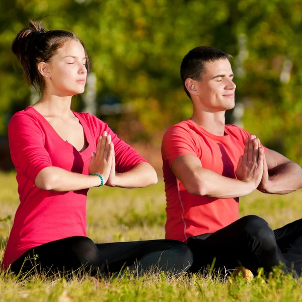 Man and woman woman doing yoga in park — Stock Photo, Image