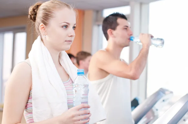 Hombre y mujer bebiendo agua después de los deportes en el gimnasio — Foto de Stock