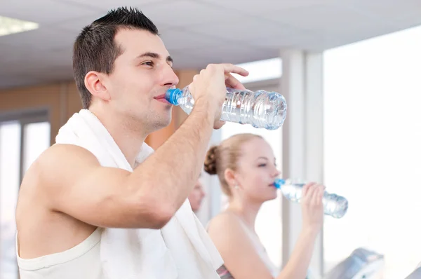 Man och kvinna dricksvatten efter sport i gym — Stockfoto