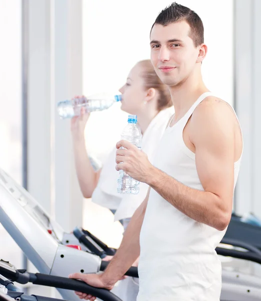 Мужчина и женщина пьют воду после занятий спортом в спортзале — стоковое фото