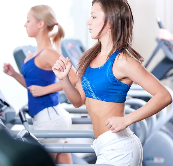 Two young women run on machine in the gym — Stock Photo, Image