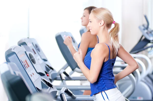 Twee jonge vrouwen draaien op machine in de sportschool — Stockfoto