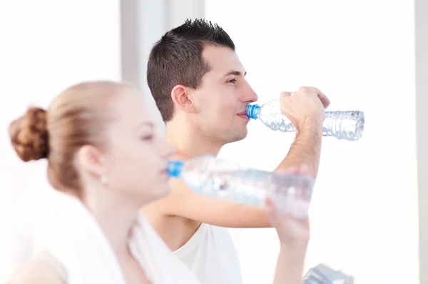 Man and woman drinking water after sports in gym — Stock Photo, Image