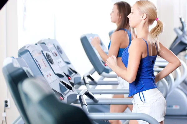 Twee jonge vrouwen draaien op machine in de sportschool — Stockfoto