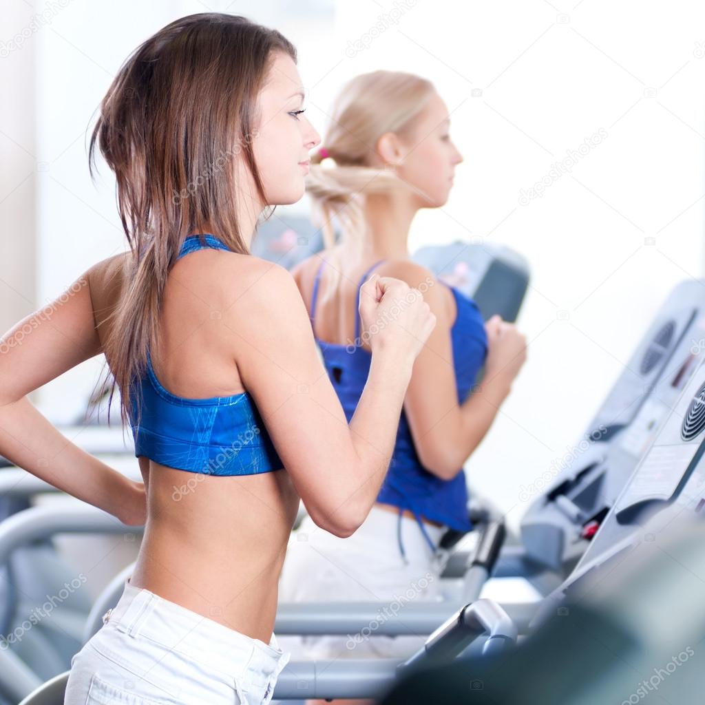 Two young women run on machine in the gym