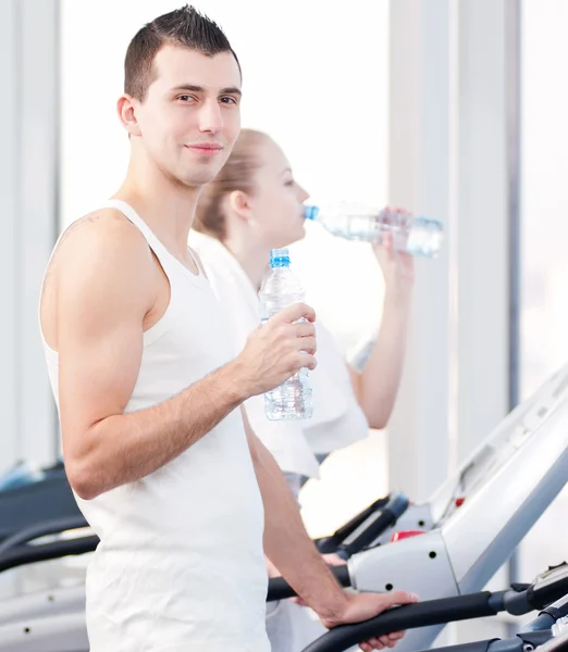 Man en vrouw drinkwater na sporten in de sportschool — Stockfoto