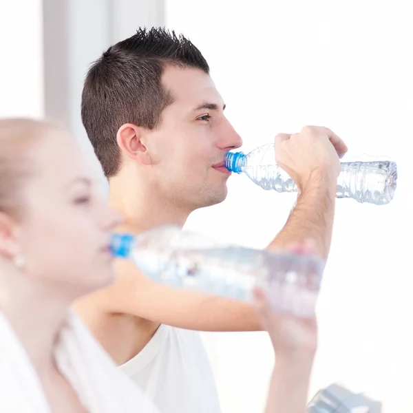 Man and woman drinking water after sports in gym — Stock Photo, Image