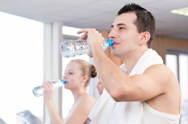 Uomo e donna che bevono acqua dopo lo sport in palestra — Foto Stock