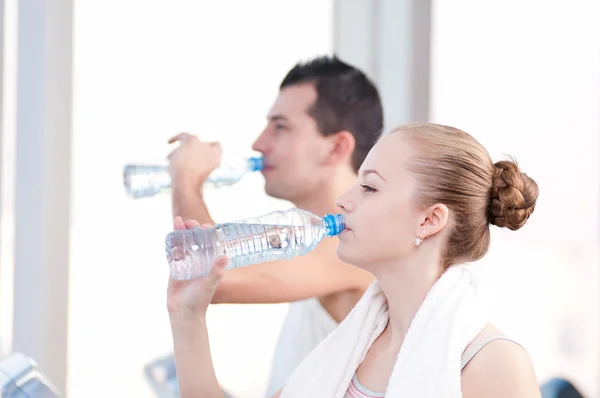 Hombre y mujer bebiendo agua después de los deportes en el gimnasio —  Fotos de Stock