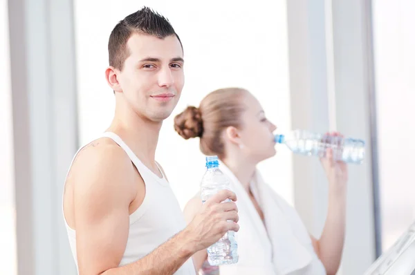 Man en vrouw drinkwater na sporten in de sportschool — Stockfoto