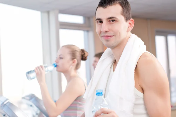 Мужчина и женщина пьют воду после занятий спортом в спортзале — стоковое фото