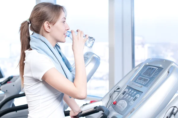 Mujer en el gimnasio haciendo ejercicio. Correr en una máquina y beber agua —  Fotos de Stock
