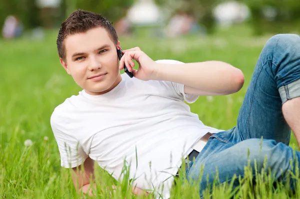 Ένας νεαρός άνδρας με το τηλέφωνο στο πράσινο city park — Φωτογραφία Αρχείου