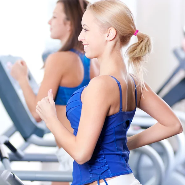 Two young women run on machine in the gym — Stock Photo, Image