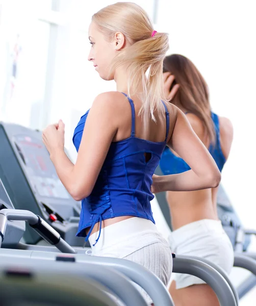 Two young women run on machine in the gym — Stock Photo, Image