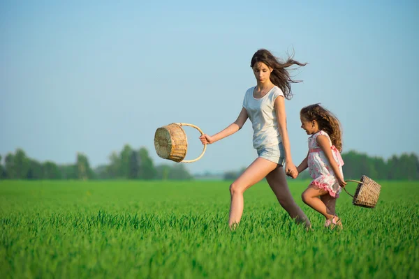 Jóvenes niñas felices corriendo cestas de brujas en el campo de trigo verde —  Fotos de Stock