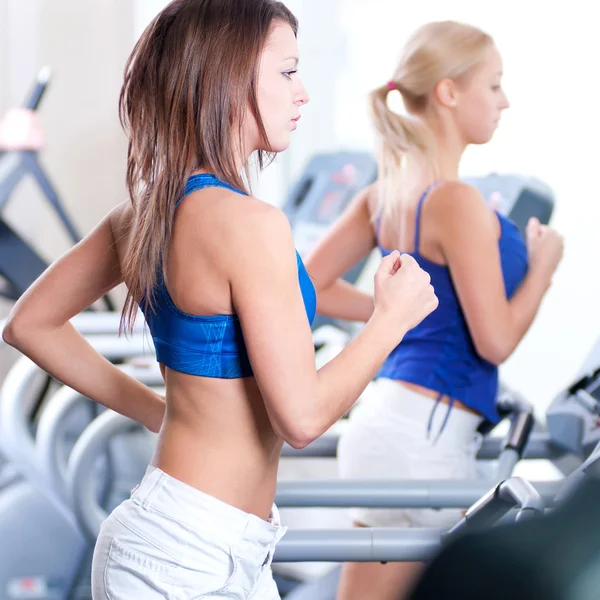 Two young women run on machine in the gym — Stock Photo, Image