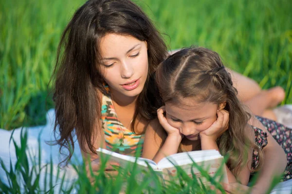 Счастливые девушки читают книгу на зеленой траве — стоковое фото