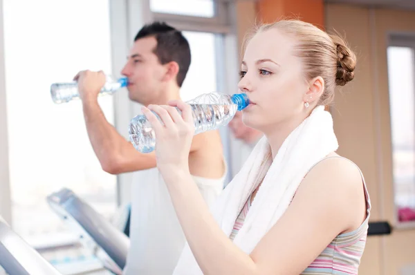 Uomo e donna che bevono acqua dopo lo sport in palestra — Foto Stock