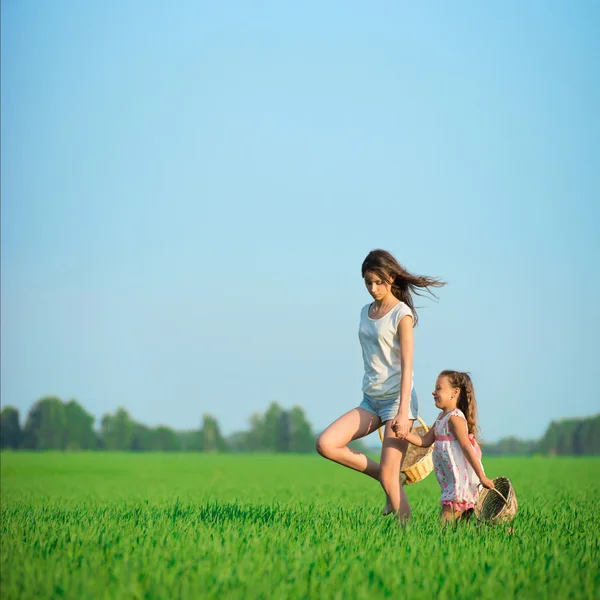 Jóvenes niñas felices corriendo cestas de brujas en el campo de trigo verde — Foto de Stock