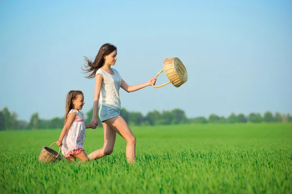 Jóvenes niñas felices corriendo cestas de brujas en el campo de trigo verde —  Fotos de Stock