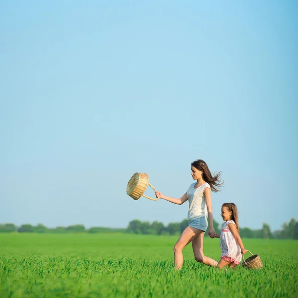 Jóvenes niñas felices corriendo cestas de brujas en el campo de trigo verde — Foto de Stock