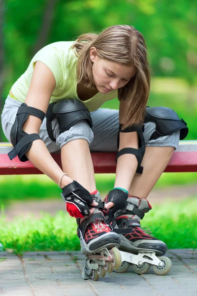 Girl going rollerblading sitting in bench putting on inline skat — Stock Photo, Image