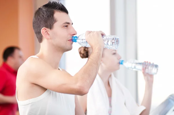 Mann und Frau trinken nach Sport in Turnhalle Wasser — Stockfoto