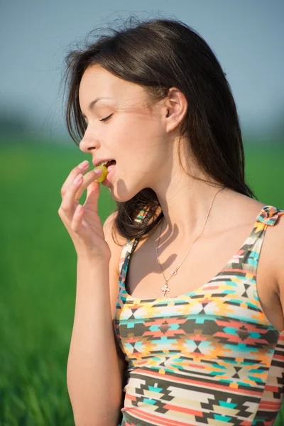 Glad tjej på grönt gräs äter druva — Stockfoto