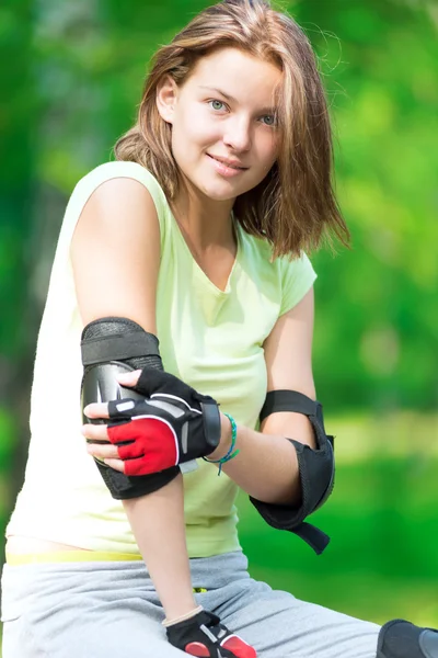 Mädchen beim Inlineskaten sitzt in Bank und legt Ellenbogenschutz an — Stockfoto