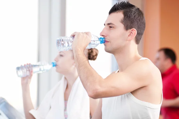 Mann und Frau trinken nach Sport in Turnhalle Wasser — Stockfoto