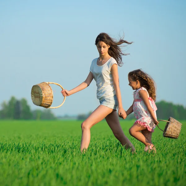 Jovens meninas felizes executando cestas de bruxa no campo de trigo verde — Fotografia de Stock