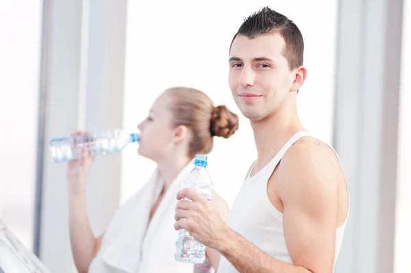 Mann und Frau trinken nach Sport in Turnhalle Wasser — Stockfoto