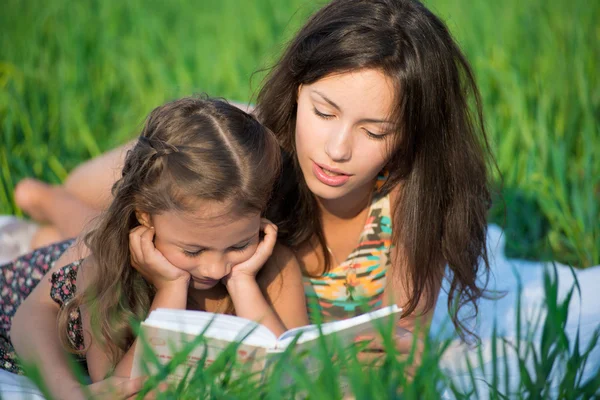 Счастливые девушки читают книгу на зеленой траве — стоковое фото