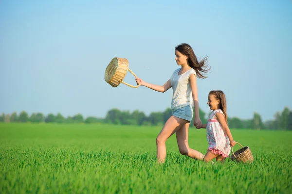 Jóvenes niñas felices corriendo cestas de brujas en el campo de trigo verde —  Fotos de Stock